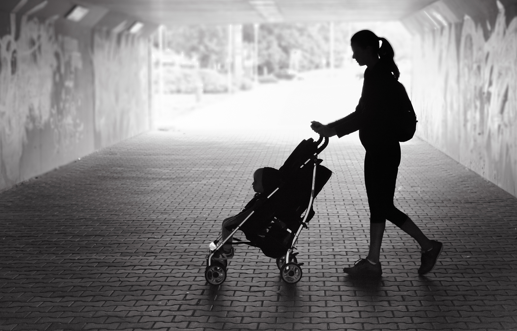 Single mother walking in city tunnel with baby in stroller.